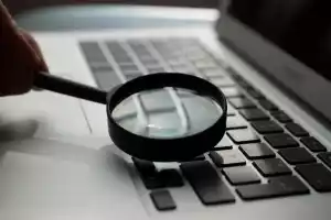 Eine schwarze Lupe wird über eine Laptop-Tastatur gehalten.