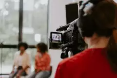 Kamerafrau filmt Personen mit einer Fernsehkamera, auf der die Videoaufnahme angezeigt wird.
