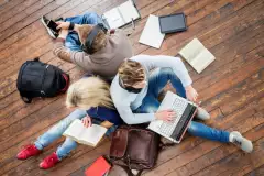 Drei Personen sitzen mit Büchern und Laptop am Boden