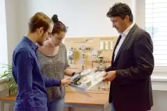 Eine Person zeigt zwei weiteren Personen ein Bauteil einer Heizungsanlage