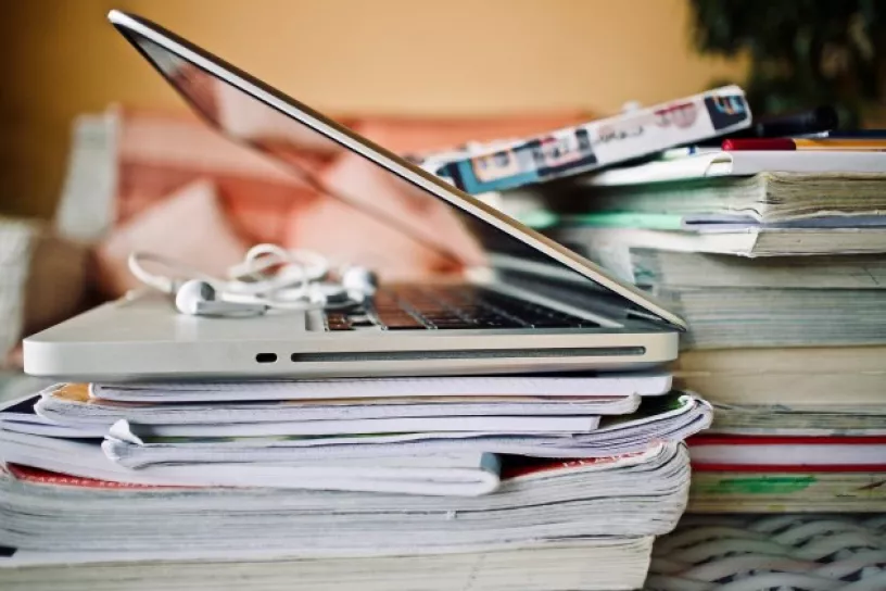Geöffneter Laptop auf einem Stapel Hefte und Bücher