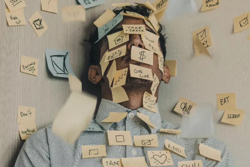 Ein Mann ist zugedeckt mit Post-its. Es wirkt als wäre er unter den Todos begraben.