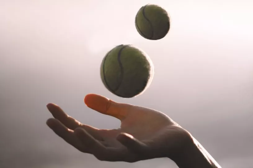 Hand, darüber schweben zwei Tennisbälle in der Luft