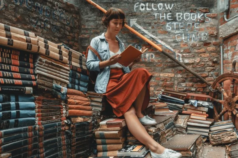 Frau sitzt auf Bücherstapel und liest