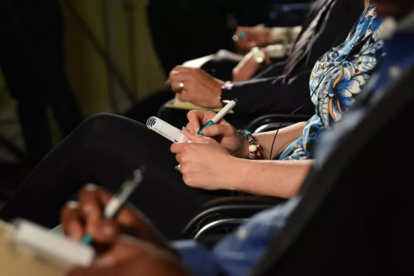Person mit Notizblock und Stift sitzt in Konferenzraum.
