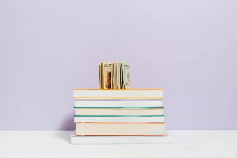 Auf einem Stapel Bücher liegen Geldscheine