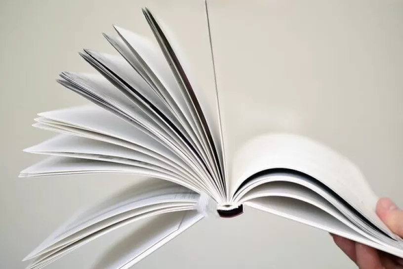 Hand hält aufgeschlagenes Buch mit aufgeblätterten Seiten