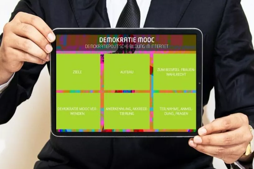 Ausschnitt einer Person im Anzug, die ein Tablet hält, das die Website des Demokratie MOOCs zeigt.