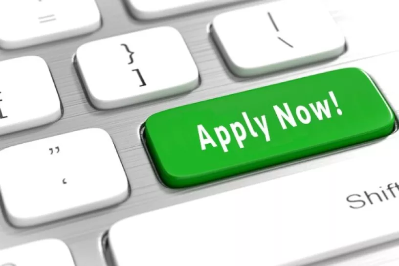Bildmontage: Auf einer Computer-Tastatur ist ein Button auf dem „Apply Now!“ steht.