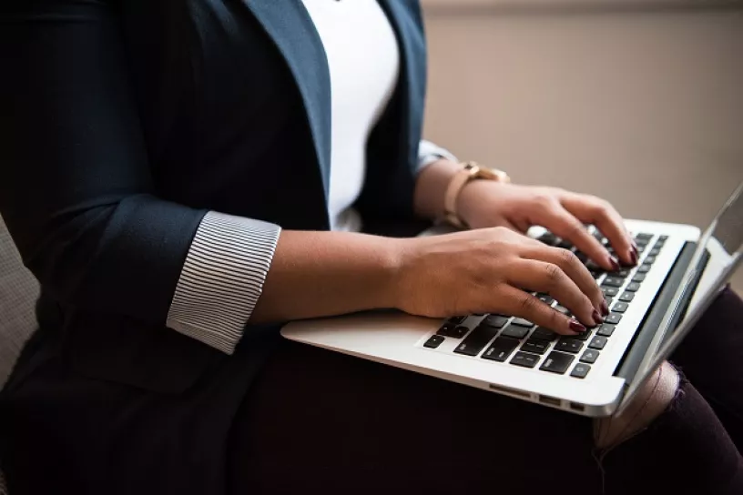 Ausschnitt einer Person mit Laptop am Schoß, die mit beiden Händen auf der Tastatur tippt