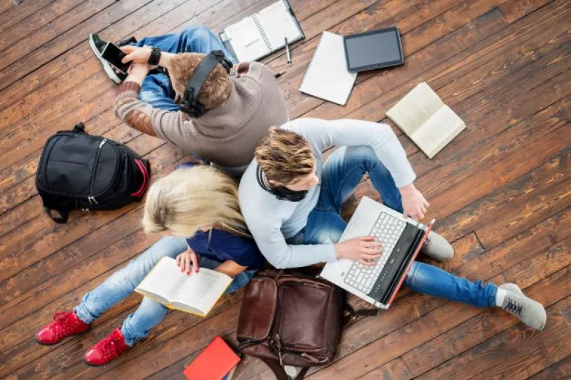 Drei Personen sitzen mit Büchern und Laptop am Boden