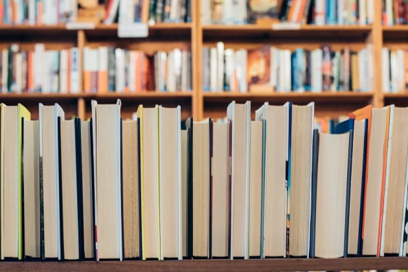 Aneinandergereihte Bücher, im Hintergrund Bücherregale einer Bibliothek