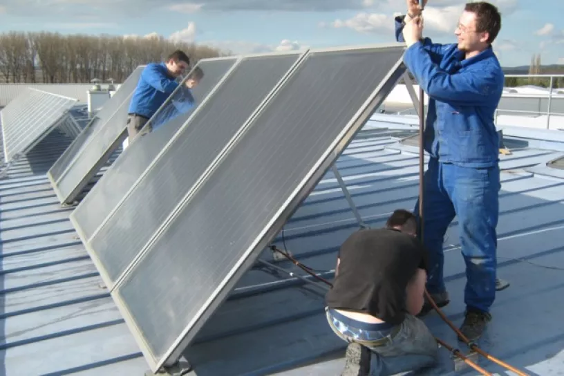Drei Männer montieren Solarpaneele auf einem Dach